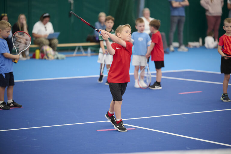 A picture of a young boy about to hit a tennis ball with his tennis racket