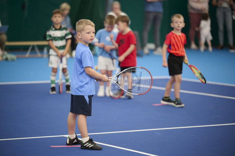 A young boy holding a tennis racket waiting to hit the ball