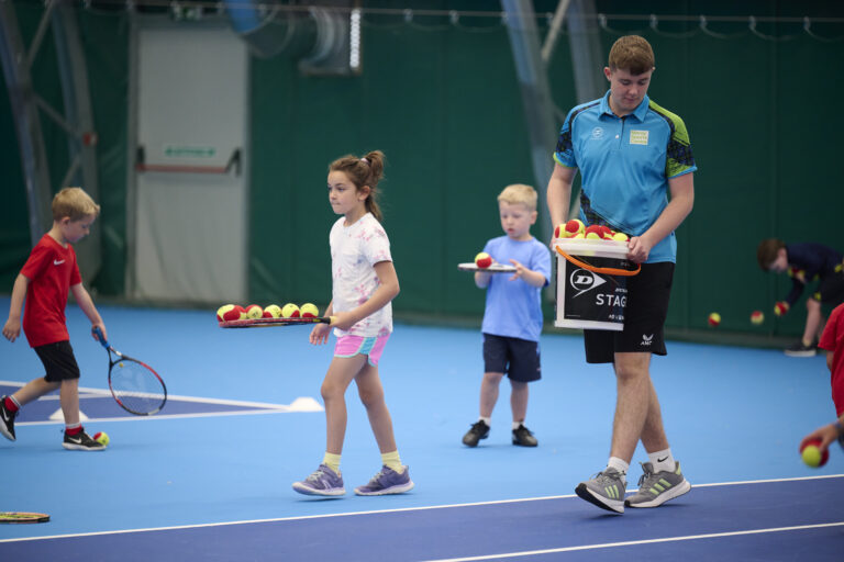 A picture of some young kids and moray sports centre staff member concentrating while balancing tennis balls on the tennis racket