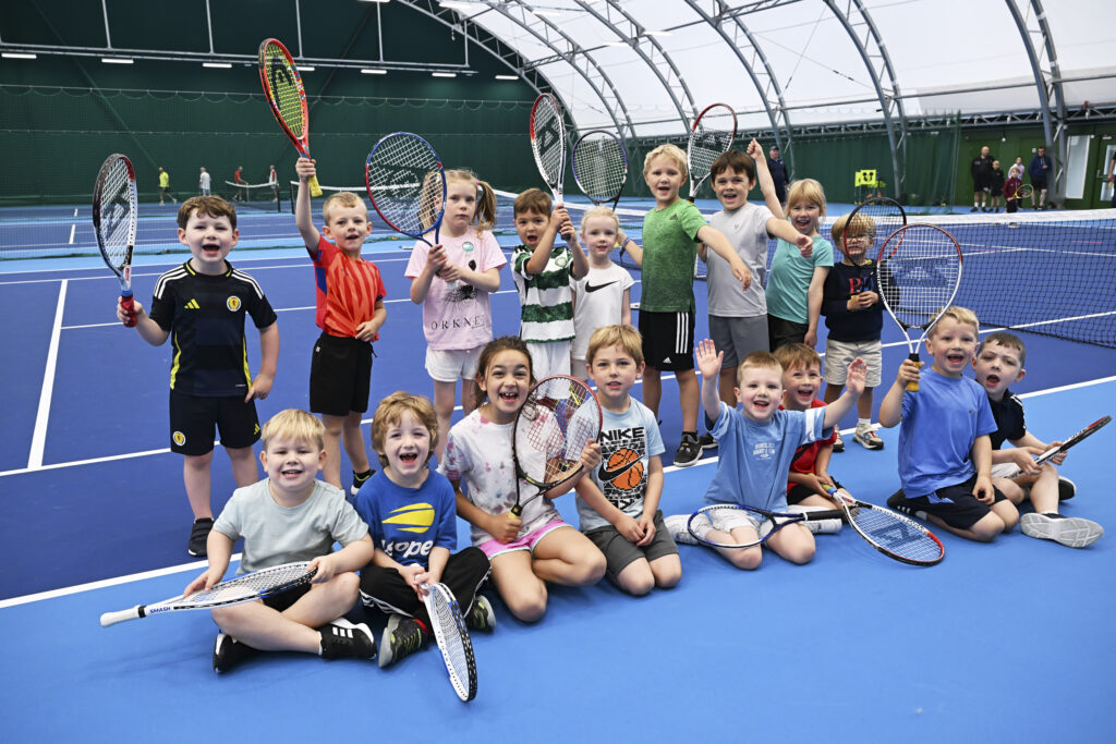 A group photo of your kids at a tennis coaching lesson holding up their tennis rackets and having fun