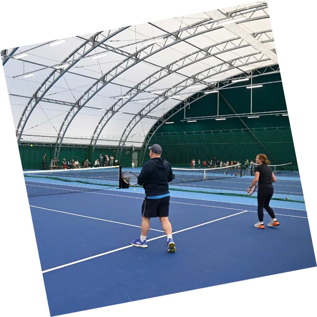 picture of two adults playing tennis in the indoor tennis court